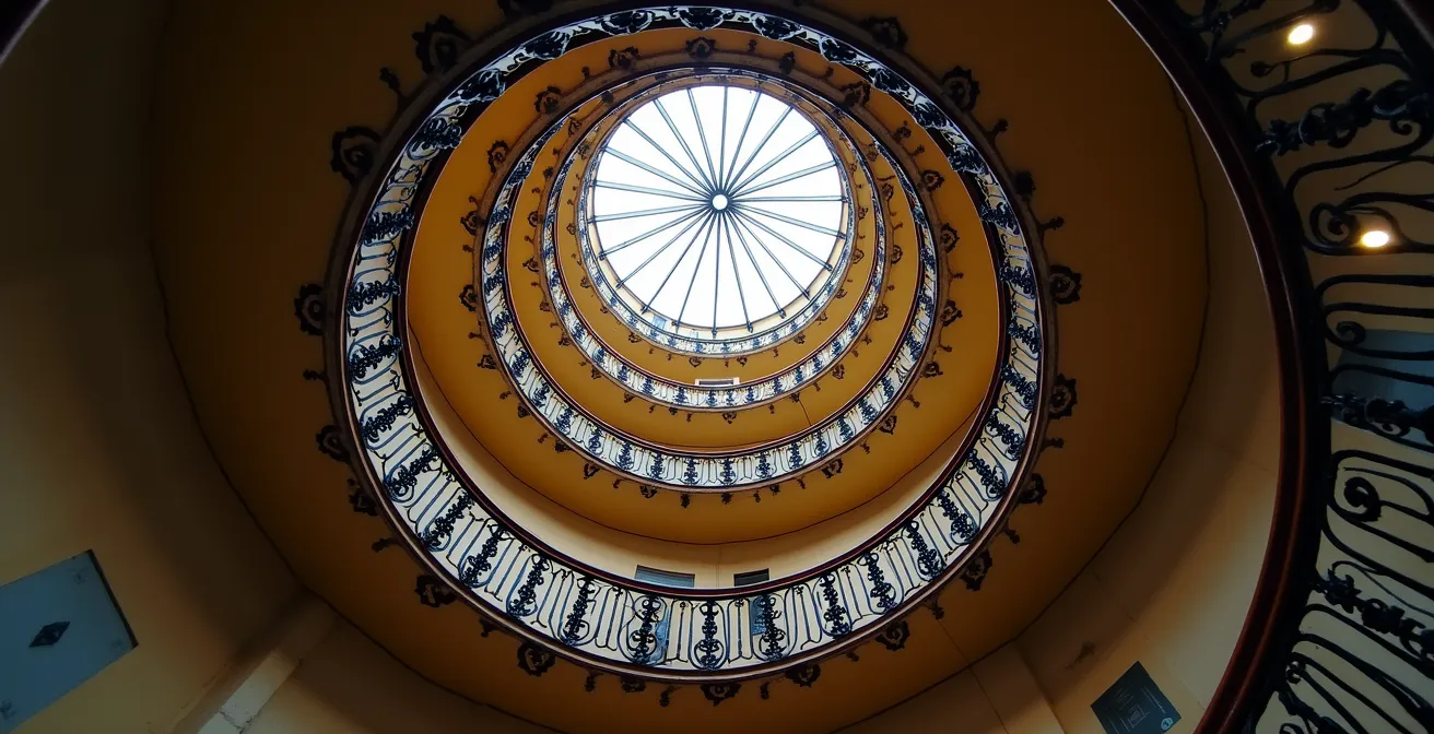 Historic wrought-iron spiral staircase inside a classic Parisian Haussmann building with ornate details